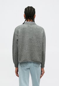 Gray wool blend sweater with dropped shoulders, a rounded neckline, and a slightly cropped fit, paired with light blue denim jeans.