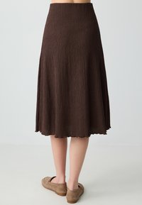 Jupe marron, longueur genou, en tissu texturé, avec une taille ajustée et un ourlet évasé à bord ondulé.