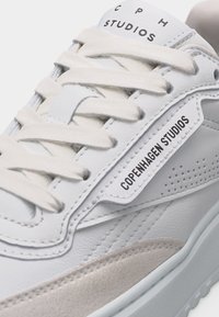 Λευκό αθλητικό παπούτσι Copenhagen Studios με μπεζ λεπτομέρεια σουέντ, λευκά κορδόνια και λογότυπο στο γλώσσα και στην πλευρική επιφάνεια.