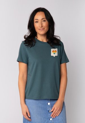 Teal shirt met korte mouwen en een hartafbeelding in regenboogkleuren op een spraakballon. Zachte stof en een relaxte pasvorm. Lichtgewicht ontwerp.