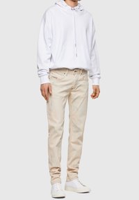Sudadera blanca con capucha y bolsillo frontal, combinada con vaqueros de mezclilla beige desgastados y zapatillas blancas con suela texturizada.
