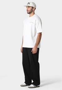 Camiseta blanca de manga corta con un pequeño detalle bordado, combinada con pantalones de pierna ancha negros y zapatillas blancas con acentos grises.