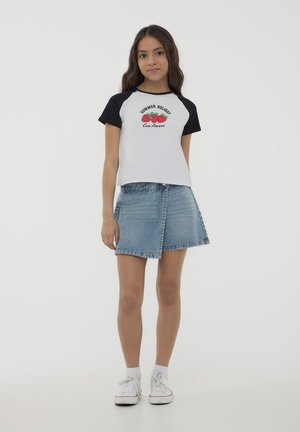 T-shirt corta bianca e nera con grafica di fragole, abbinata a una gonna in denim chiaro e sneakers bianche con calzini arrotolati.