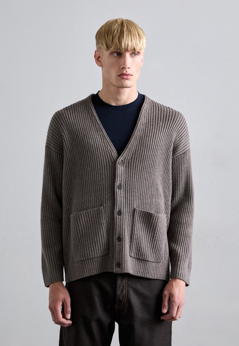Grå ribbad cardigan med V-hals, knäppning fram och två framfickor. Tillverkad av mjukt material med en texturerad yta.