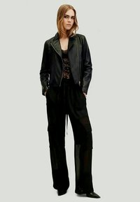 Jaqueta de couro preta sobre um top de renda preta, combinada com calças largas e soltas pretas. O outfit apresenta uma silhueta elegante e uma textura suave.