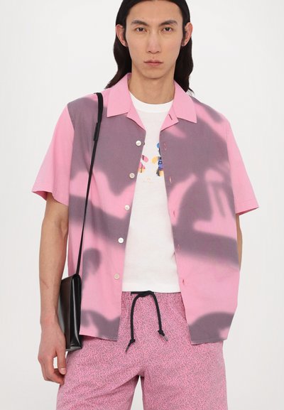 Korte mouwen shirt met een roze en grijze gradient ontwerp, met knoppen, gedragen over een wit graphic T-shirt, gecombineerd met een gebloemde short.