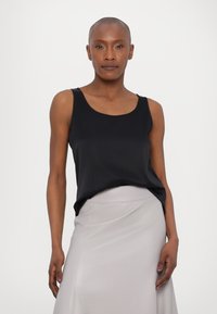 Black sleeveless top with a round neckline, made of smooth fabric, paired with a light gray, fitted skirt. Simple and clean design.