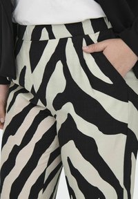 Zwart-witte zebraprint broek gemaakt van lichte stof, met een hoge taille en zijzakken. Glad textuur en wijde pasvorm.