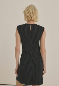 Musthave mustasustime, millel on vertikaalsed valged triibud, lühikesed varrukad ja väike võtiava taga. Sile kangas ja keha lähedane siluett.