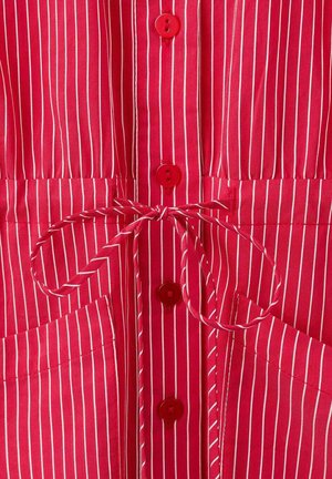 Tissu rayé rouge avec des lignes verticales blanches, comportant des boutons rouges, une taille nouée et deux poches avant. Texture lisse.