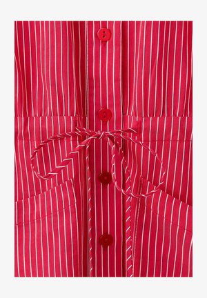 Tkanina crvenih pruga s bijelim okomitim linijama, s crvenim gumbima, vezanim strukom i dva prednja džepa. Glatka tekstura.