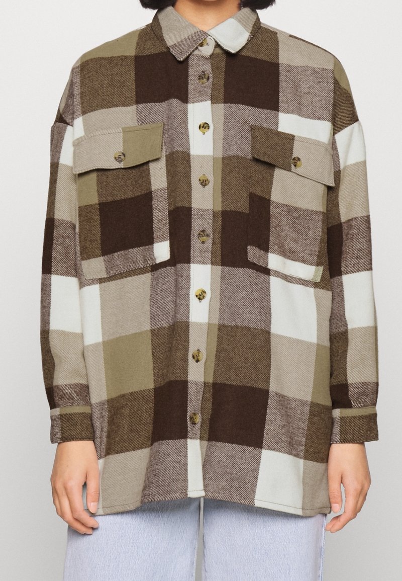 Rutigt skjorta i brunt, krämfärgat och olivgrönt. Har två bröstfickor, krage och knappar framtill. Mjuk tygtextur.