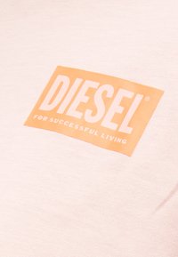 Λογότυπο DIESEL σε λευκό χρώμα πάνω σε πορτοκαλί ορθογώνιο φόντο με το κείμενο "FOR SUCCESSFUL LIVING" σε απαλό ροζ ύφασμα.