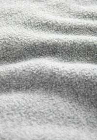 Tela de forro de color gris claro con una superficie suave y texturizada, formando suaves ondas y ondulaciones, mostrando un color uniforme sin patrones.