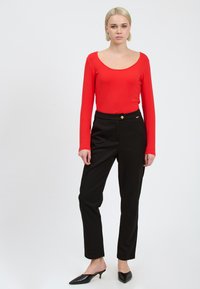 Rode lange mouwen top met een ronde hals, gecombineerd met zwarte slim-fit broeken met een gouden accent op de taille en zwarte puntige hakken.