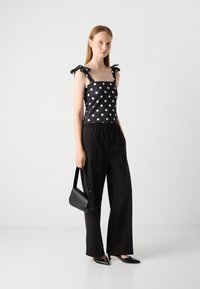 Black polka dot top with shoulder bows, worn with black wide-leg trousers and pointed heels. Complemented by a black handbag.