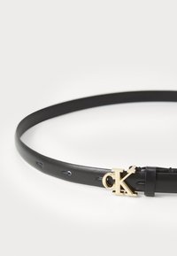 Zwarte leren riem met gouden "CK" metalen accent, met een gladde textuur, slank ontwerp en meerdere gaten voor verstelbaarheid.