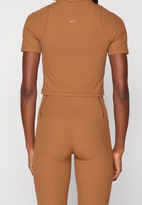 Woman wearing fitted ribbed tan short-sleeve crop top and high-waisted leggings, back view, with small white Nike logo on top.