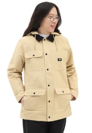 Giacca beige con cappuccio, dotata di due ampie tasche frontali, bottoni a pressione neri e colletto in corduroy. Presenta una vestibilità rilassata e materiale resistente.