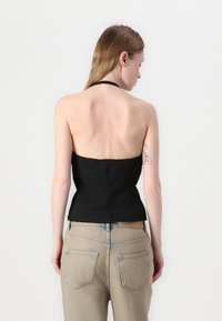 Svart halter-top med fitted design, glatt tekstur og rett nederkant, kombinert med lysvaskede denimjeans med baklommer.