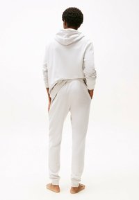 Hellgrauer Hoodie mit lockerer Passform, ausgestattet mit einem Kordelzug am Hals. Kombiniert mit passenden Jogginghosen, beide aus weichem, glattem Stoff.
