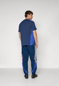 T-shirt azul marinho de manga curta com painéis laterais azuis, combinado com calças de treino azul marinho com riscas vermelhas e brancas e cintura elástica.