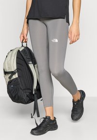 Γκρι κολάν με λογότυπο, μαύρα αθλητικά παπούτσια και διχρωμικό σακίδιο πλάτης. Το σύνολο διαθέτει απλό σχεδιασμό και κομψή, εφαρμοστή γραμμή.