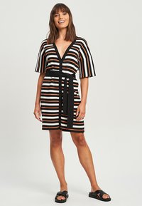 Prugasta obleka z V-izrezom, kratkimi rokavi in pasom. Ima črne, oranžne in bele vodoravne stripe. Iz lahke pletenine.