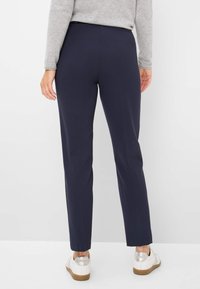 Navy stretchbroeken met een slim fit, platte voorkant en twee achterzakken, gecombineerd met witte sneakers met zilveren accenten.
