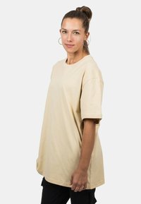 Beige oversized t-shirt made of cotton. Short sleeves, round neckline, soft texture. Worn by a person with hair tied back.