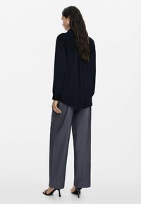 Marineblauwe blouse met lange mouwen en een ontspannen pasvorm, gecombineerd met grijze broek met brede pijpen met een geborduurd bloemmotief aan de zijkant.