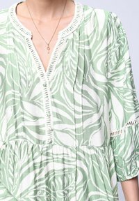 Robe verte et blanche à motifs, avec un col en V, des détails de boutons, des manches trois-quarts et une texture froncée au niveau de la taille.