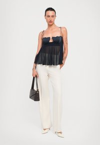 Top negro semitransparente con diseño de escote en forma de scallop, combinado con pantalones blancos ajustados, bolso negro de hombro y tacones puntiagudos en color blanco roto.