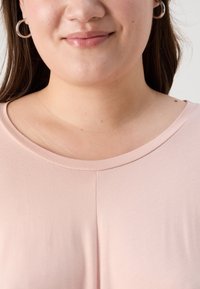 Απαλή ροζ κοντομάνικη μπλούζα φτιαγμένη από μαλακό, ελαστικό ύφασμα με στρογγυλή λαιμόκοψη και διακριτές ραφές μπροστά.