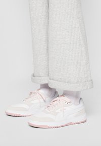 Baskets blanches et roses avec des textures lisses et en daim, dotées de lacets et de semelles en caoutchouc, associées à un pantalon en maille ribbed gris clair.