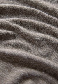 Tekstūrēts pelēks audums parāda mīkstu, nedaudz pūkainu virsmu ar maigiem viļņiem un krokām, izceļot tā vieglo un elastīgo raksturu.