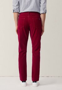Dieprode korduroy broek met een rechte pasvorm, voorzien van een achterzakontwerp, gecombineerd met witte sneakers. Verticale gestreepte shirt zichtbaar.