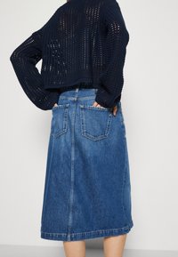 Falda en línea A de denim en azul medio con cintura alta y dos bolsillos traseros. La tela tiene una textura suave y un dobladillo a la altura de la rodilla.