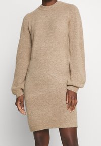Abito maglione beige a maglia con scollo a girocollo, maniche lunghe a palloncino e polsini a coste. Texture morbida, lunghezza midi.