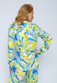 Bluzka i spodnie w kolorowe wzory w jasnym niebieskim, żółtym i beżowym, z wirującymi wzorami oraz gładką, lekką teksturą materiału.