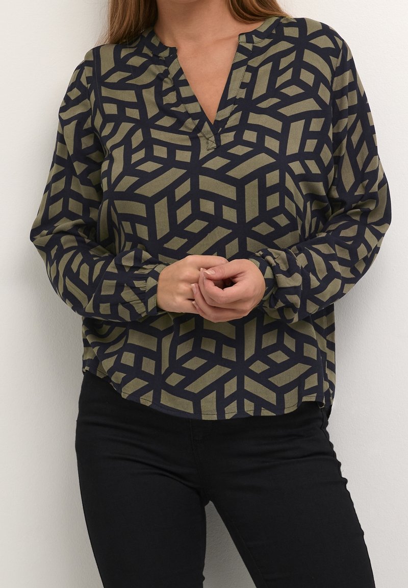 Blouse à manches longues en vert olive et marine, présentant un motif géométrique, un décolleté en V et des poignets froncés. Texture lisse et coupe décontractée.