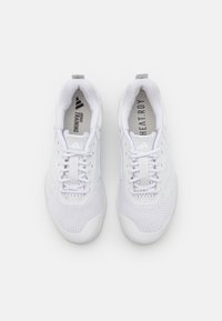 Baskets de sport blanches en tissu en maille, avec fermeture à lacets et logo embossé sur la languette. Présente des détails texturés sur les côtés.