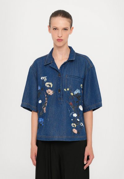 Chemise en denim à manches courtes, ornée de broderies florales en rose, bleu et blanc. Comprend une poche avant et une fermeture à boutons.