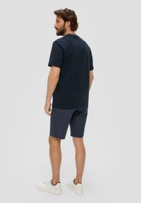 Granatowa koszulka z krótkim rękawem o okrągłym dekolcie, zestawiona z wzorzystymi ciemnoniebieskimi szortami i białymi trampkami. Prosty, codzienny design.