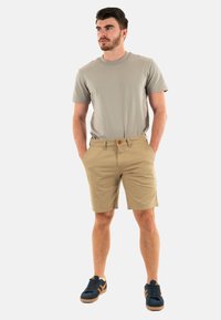 Camiseta gris claro, pantalones cortos caqui y zapatillas deportivas azul marino. Tejido de algodón, mangas cortas y escote redondo. Corte casual con bolsillos.