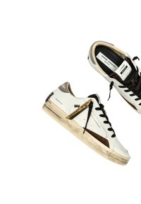Sneakers in pelle bianca con suola in gomma beige, lacci neri e dettagli in suede marrone. Presentano un'etichetta con il marchio sul lato.