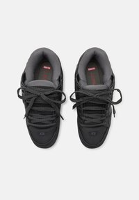 Black sneakers with a leather and mesh upper, textured dark gray laces, padded tongue, and logo detail on the side.