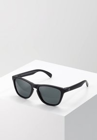 Ochelari de soare negri cu lentile închise la culoare, ramă pătrată și material plastic elegant. Prezintă un branding minim pe braț.