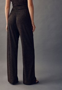 Čierne nohavice s širokými nohavicami z textúrovaného materiálu s jemnými trblietavými akcentmi. Majú elastický pás pre pohodlie a uvoľnený strih.