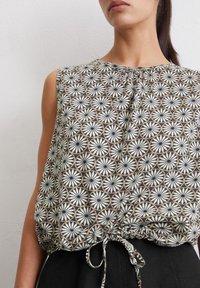 Hihaton toppi kevyestä kankaasta, jossa on mustavalkobeige-geometrinen kuvio, ja vyötäröllä kiristysnauha.